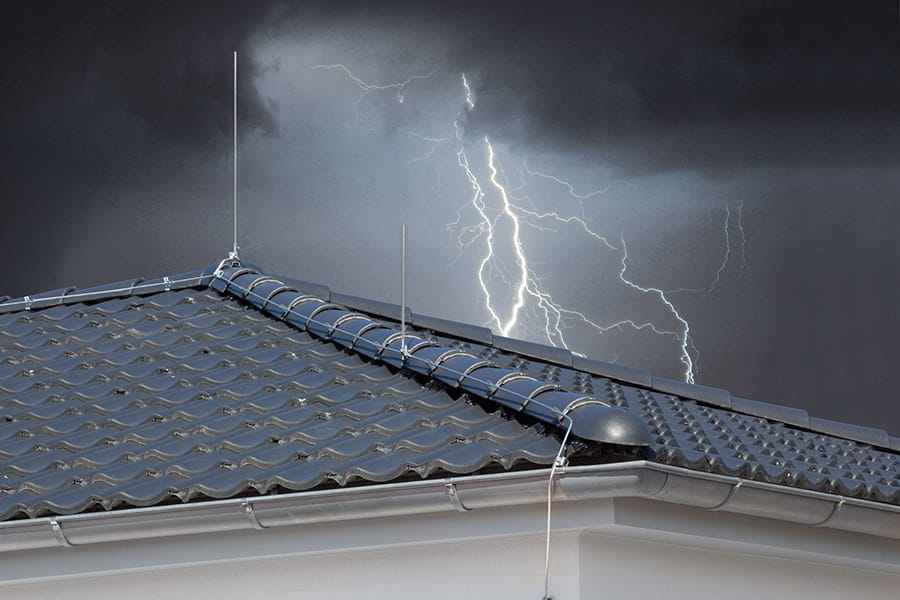 Ein mit Blitzableitern ausgestattetes Dach. Im Hintergrund sind Gewitterwolken und ein Blitz zu sehen.