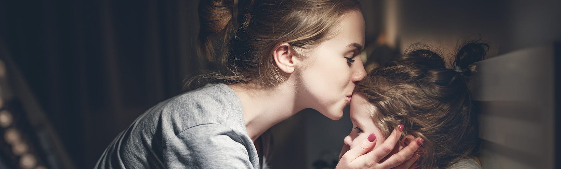 Eine Frau küsst ihrem Kind auf die Stirn